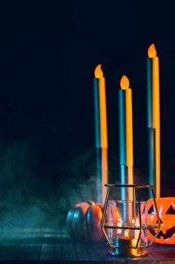 Cadılar Bayramı konsepti, mum ve mumluk kadar aydınlatma ile ürkütücü süslemeleri koyu ahşap bir masa etrafında yeşil tonu duman ile, yakın.