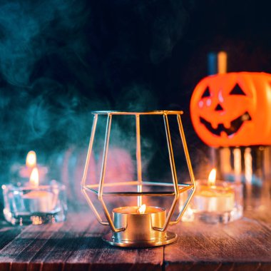 Cadılar Bayramı konsepti, mum ve mumluk kadar aydınlatma ile ürkütücü süslemeleri koyu ahşap bir masa etrafında yeşil tonu duman ile, yakın.