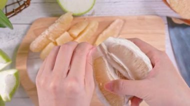 Genç asyalı kadın parlak beyaz ahşap masa ve doğrama tahtası üzerinde ev mutfağında yemek için taze pomelo soyma, üst görünümü, havai görünüm, yaşam tarzı.