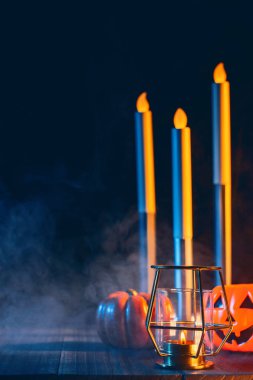 Cadılar Bayramı konsepti, mum ve mumluk kadar aydınlatma ile ürkütücü süslemeleri koyu ahşap bir masa etrafında mavi sesi duman, yakın.