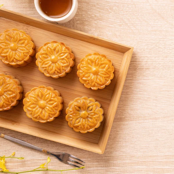 Moon cakes with tea on bright wooden table and serving try, holiday concept of Mid-Autumn festival traditional food layout design, close up, copy space.