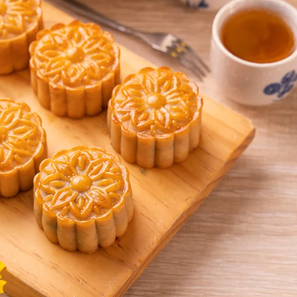 Moon cakes with tea on bright wooden table and serving try, holiday concept of Mid-Autumn festival traditional food layout design, close up, copy space.