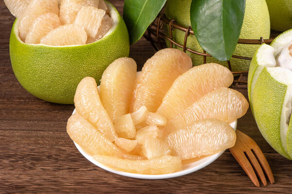 Fresh peeled pomelo, grapefruit, shaddock with green leaves on dark wooden plank table. Seasonal fruit near mid-autumn festival, close up, copy space