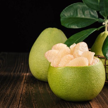 Taze soyulmuş pomelo, greyfurt, koyu ahşap tahta masada yeşil yaprakları ile gölgeli. Sonbahar ortası festivaline yakın mevsim meyveleri, yakın çekim, kopyalama alanı