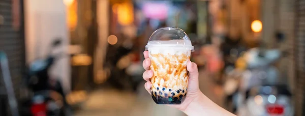 Genç kız tutuyor ve Tayvan arka plan gece pazarında kahverengi şeker aromalı tapyoka inci kabarcık süt çayı bir fincan gösteren, yakın, bokeh — Stok fotoğraf