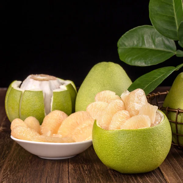 Fresh peeled pomelo, grapefruit, shaddock with green leaves on dark wooden plank table. Seasonal fruit near mid-autumn festival, close up, copy space — Stock Photo, Image