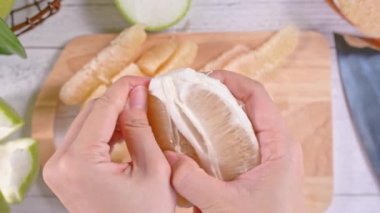 Genç asyalı kadın parlak beyaz ahşap masa ve doğrama tahtası üzerinde ev mutfağında yemek için taze pomelo soyma, üst görünümü, havai görünüm, yaşam tarzı.