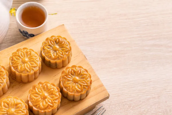 Moon cakes with tea on bright wooden table and serving try, holiday concept of Mid-Autumn festival traditional food layout design, close up, copy space.