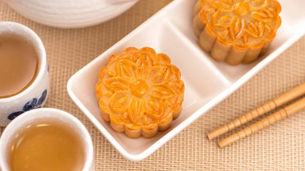 Moon cakes with tea on bright wooden table and serving try, holiday concept of Mid-Autumn festival traditional food layout design, close up, copy space.