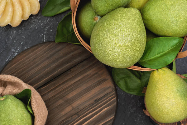 Fresh pomelo, grapefruit in bamboo basket with green leaf on dark black slate background. Seasonal fruit for Mid-Autumn Festival. Top view. Flat lay.