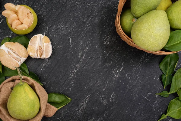 Fresh pomelo, grapefruit in bamboo basket with green leaf on dark black slate background. Seasonal fruit for Mid-Autumn Festival. Top view. Flat lay. — Stock Photo, Image