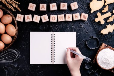 Genç kadın okuma ve Cadılar Bayramı çerezleri yapma tarifi yazıyor, Cadılar Bayramı partisi için hazırlanıyor tasarım kavramı, üstgörünüm, düz yatıyordu, havai.