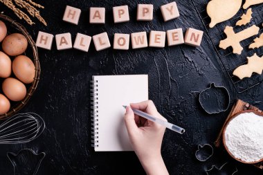 Genç kadın okuma ve Cadılar Bayramı çerezleri yapma tarifi yazıyor, Cadılar Bayramı partisi için hazırlanıyor tasarım kavramı, üstgörünüm, düz yatıyordu, havai.