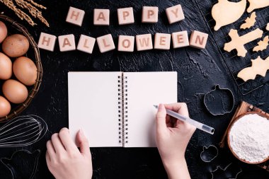 Genç kadın okuma ve Cadılar Bayramı çerezleri yapma tarifi yazıyor, Cadılar Bayramı partisi için hazırlanıyor tasarım kavramı, üstgörünüm, düz yatıyordu, havai.