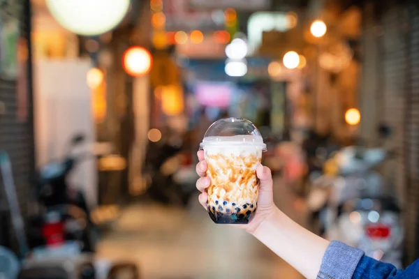 Chica joven en chaqueta de mezclilla está bebiendo azúcar morena con sabor a tapioca perla té de leche de burbuja con paja de vidrio en el mercado nocturno de Taiwán, de cerca, bokeh — Foto de Stock