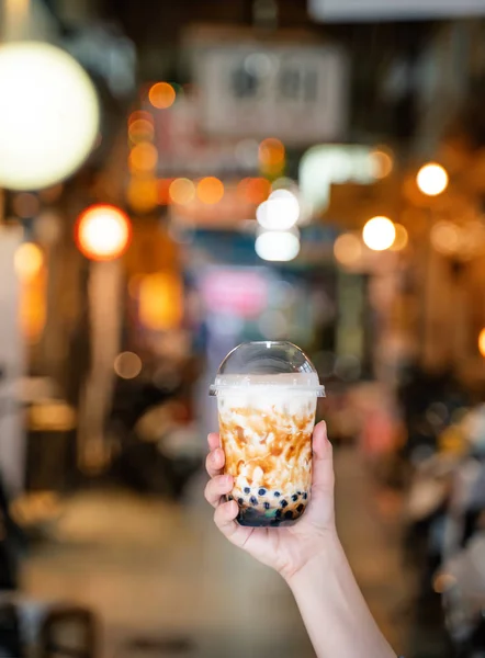 Chica joven en chaqueta de mezclilla está bebiendo azúcar morena con sabor a tapioca perla té de leche de burbuja con paja de vidrio en el mercado nocturno de Taiwán, de cerca, bokeh — Foto de Stock