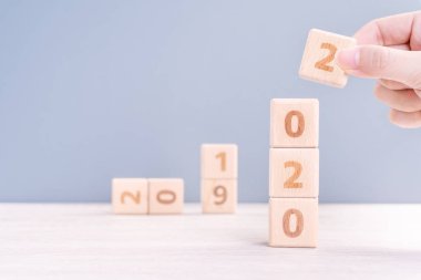 Soyut 2020 & 2019 Yeni yıl geri sayım tasarım konsepti - ahşap masa ve mavi arka plan üzerinde ahşap blokküpler tutan kadın, yakın çekim, kopyalama alanı.