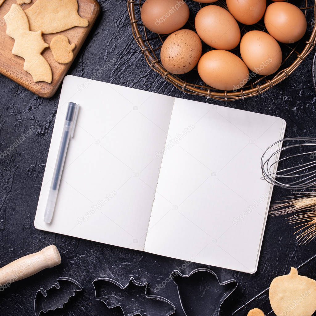 Woman is reading cookbook recipe of making Halloween cookies with baking ingredients, design concept of cooking class, top view, flat lay, overhead.