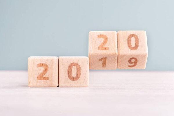 Abstract 2020 & 2019 New year countdown design concept - wood blocks cubes on wooden table and low saturation green background, close up, copy space.