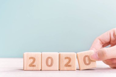 Soyut 2020 & 2019 Yeni yıl geri sayım tasarım konsepti - ahşap masa ve yeşil arka plan üzerinde ahşap blokküpler tutan kadın, yakın, kopyalama alanı.