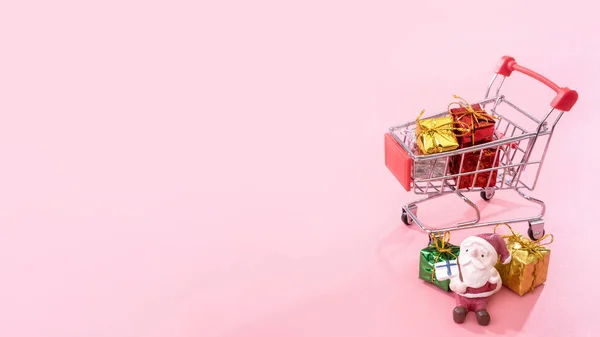 Concepto de compras de Navidad, mini carrito de la tienda roja con juguete de Santa Claus y caja de regalo aislado sobre fondo rosa pálido, espacio de copia en blanco, primer plano —  Fotos de Stock