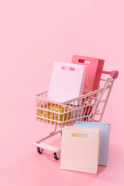 Concepto de temporada de compras de venta anual - mini carrito de la tienda roja lleno de regalo bolsa de papel aislado sobre fondo rosa pálido, espacio de copia en blanco, primer plano —  Fotos de Stock