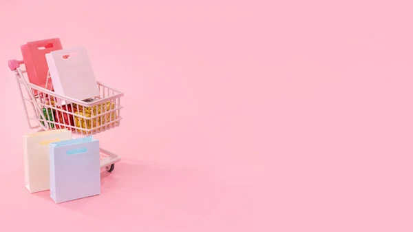 Ежегодная концепция торгового сезона - тележка с тележкой из мини-красного магазина, заполненная подарком из бумажного пакета, изолированная на бледно-розовом фоне, пустое пространство для копирования, закрыть — стоковое фото