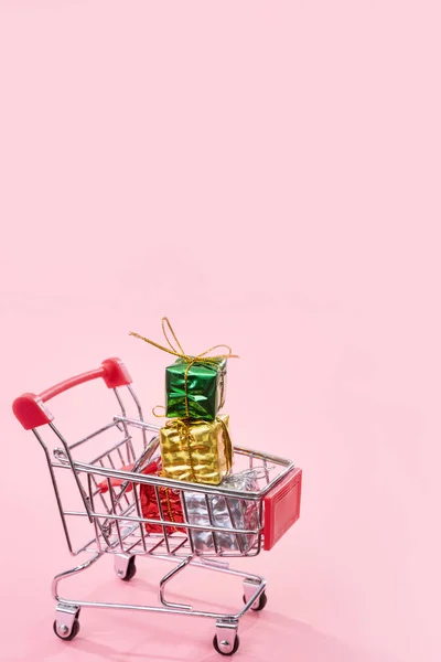 Jaarlijkse verkoop, kerst shopping seizoen concept-mini rode winkel kar trolley vol met geschenk doos geïsoleerd op bleke roze achtergrond, kopieer ruimte, close-up — Stockfoto