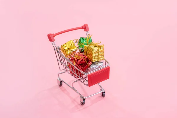 Jaarlijkse verkoop, kerst shopping seizoen concept-mini rode winkel kar trolley vol met geschenk doos geïsoleerd op bleke roze achtergrond, kopieer ruimte, close-up — Stockfoto