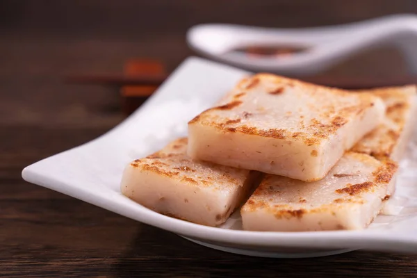 Delicious turnip cake, Chinese traditional local dish radish cake in restaurant with soy sauce and chopsticks, close up, copy space.