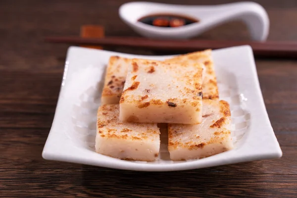 Delicious turnip cake, Chinese traditional local dish radish cake in restaurant with soy sauce and chopsticks, close up, copy space.