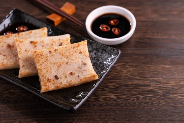 Delicious turnip cake, Chinese traditional local dish radish cake in restaurant with soy sauce and chopsticks, close up, copy space.