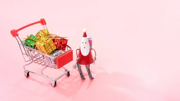 Kerst winkelen concept, mini rode winkel kar trolley met Santa Claus speelgoed en geschenk doos geïsoleerd op bleke roze achtergrond, lege kopie ruimte, close-up — Stockfoto