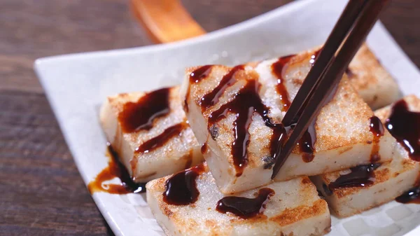 Pouring black soy sauce on ready-to-eat delicious turnip cake, Chinese traditional local dish radish cake in restaurant, close up, copy space.