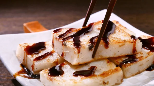 Pouring black soy sauce on ready-to-eat delicious turnip cake, Chinese traditional local dish radish cake in restaurant, close up, copy space.