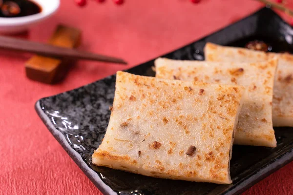 Chinese lunar new year food concept, Delicious turnip radish cake, local cuisine in restaurant with soy sauce on red background, close up, copy space