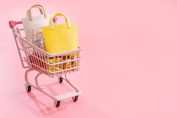 Concepto de temporada de compras de venta anual - mini carrito de la tienda roja lleno de regalo bolsa de papel aislado sobre fondo rosa pálido, espacio de copia en blanco, primer plano —  Fotos de Stock