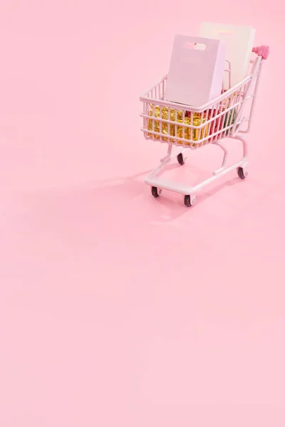 Conceito de temporada de compras de venda anual - carrinho de carrinho de loja vermelho mini cheio de presente de saco de papel isolado em fundo rosa pálido, espaço em branco cópia, close-up — Fotografia de Stock