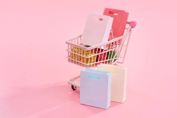 Vente annuelle concept de saison d'achat - mini chariot de chariot de magasin rouge plein de sac en papier cadeau isolé sur fond rose pâle, espace de copie vierge, gros plan — Photo