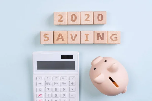 Abstract 2020 financial goal design concept - geometric wood blocks cubes on blue table background with piggy bank, top view, flat lay, copy space.