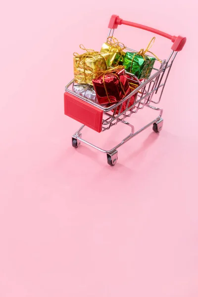 Éves értékesítése, karácsonyi vásárlási szezon koncepció-mini piros bolt kocsi kocsi tele díszdobozban izolált halvány rózsaszín háttér, másolás tér, közelről — Stock Fotó