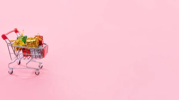 Jaarlijkse verkoop, kerst shopping seizoen concept-mini rode winkel kar trolley vol met geschenk doos geïsoleerd op bleke roze achtergrond, kopieer ruimte, close-up — Stockfoto