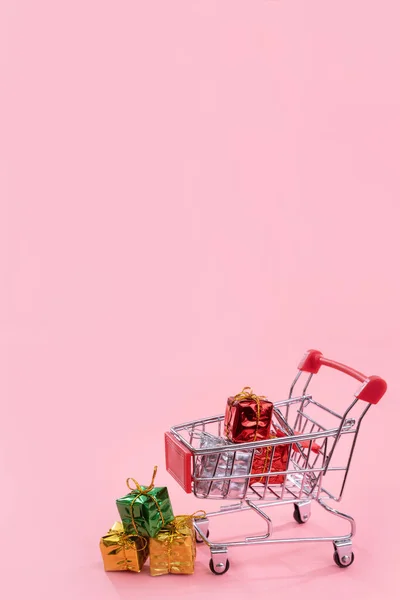 Jaarlijkse verkoop, kerst shopping seizoen concept-mini rode winkel kar trolley vol met geschenk doos geïsoleerd op bleke roze achtergrond, kopieer ruimte, close-up — Stockfoto