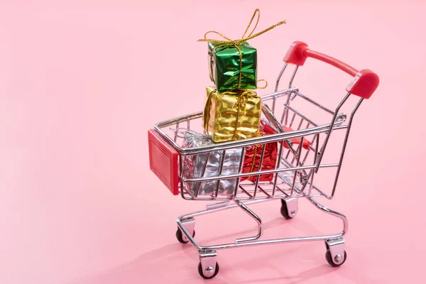Jaarlijkse verkoop, kerst shopping seizoen concept-mini rode winkel kar trolley vol met geschenk doos geïsoleerd op bleke roze achtergrond, kopieer ruimte, close-up — Stockfoto
