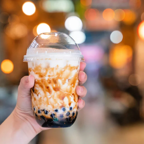 Mujer joven está sosteniendo, beber azúcar moreno con sabor a tapioca perla té de leche de burbuja con paja de vidrio en el mercado nocturno de Taiwán, de cerca, bokeh — Foto de Stock