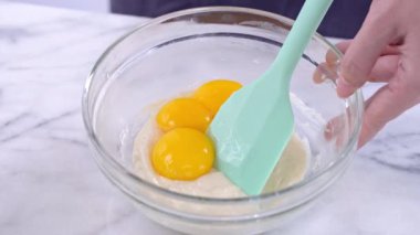 Yumurta sarısını Chiffon kek hamuru ile yeşil silikon spatula karıştırma aracı karıştırarak pürüzsüz ve iyi karıştırın cam bir kasede, 4k yakın görünüm.