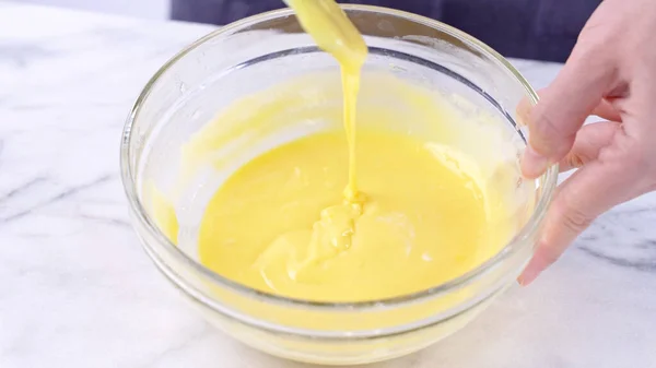 Mixing egg yolk into cake batter with green rubber spatula mixer tool stirring until smooth and blend well in a glass bowl, close up, lifestyle — Stock Photo, Image