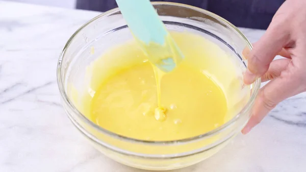 Mixing egg yolk into cake batter with green rubber spatula mixer tool stirring until smooth and blend well in a glass bowl, close up, lifestyle — Stock Photo, Image