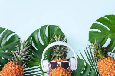 Beyaz kulaklık takan komik ananas, müzik dinleme konsepti, tropik palmiye yaprakları ile izole edilmiş renkli arka plan, üst görünüm, düz dizayn.
