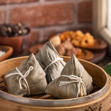 Rice dumpling - Chinese zongzi food in a steamer on wooden table with red brick wall, window background at home for Dragon Boat Festival concept, close up.
